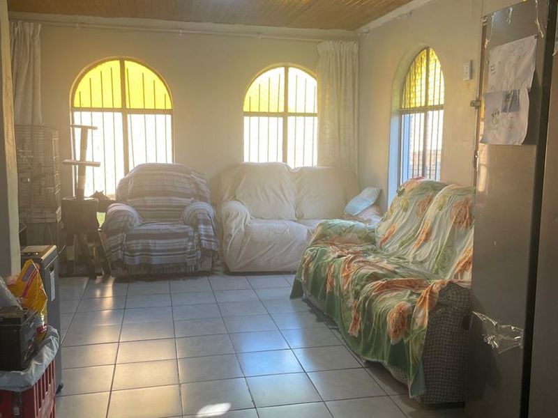 A living room featuring tiled flooring, a timber-clad ceiling, and three arched windows with security bars.