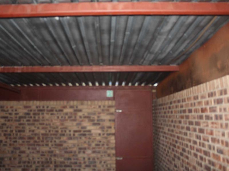 An empty garage space featuring exposed steel beams, a corrugated metal roof, and facebrick walls, showing signs of wear and aging.