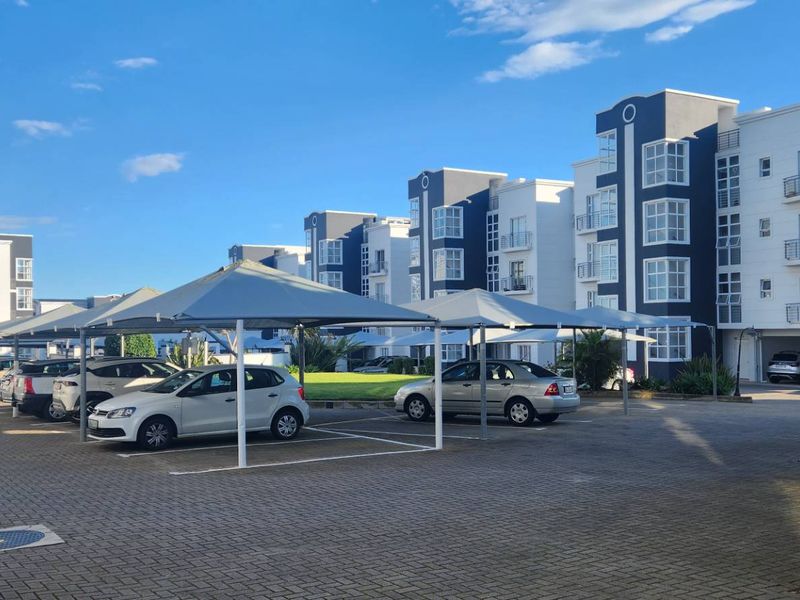 Exterior view of a modern apartment complex featuring paved parking areas with shade-cloth carports and well-maintained multi-story residential buildings.