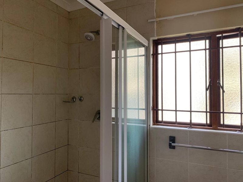 A functional bathroom featuring a shower enclosure with tiled walls and a window fitted with security bars.