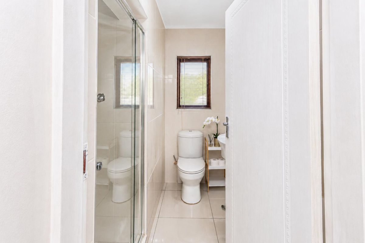 A compact, well-maintained bathroom featuring a glass-enclosed shower, ceramic tiling, and a window for natural light.