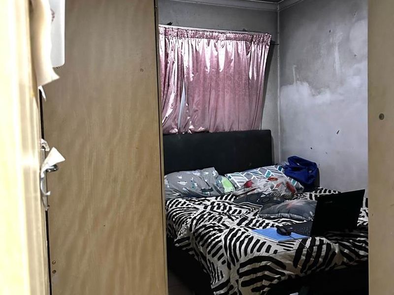 A compact bedroom featuring tiled flooring and a ceiling light fixture, currently requiring significant wall repairs and cosmetic refurbishment.