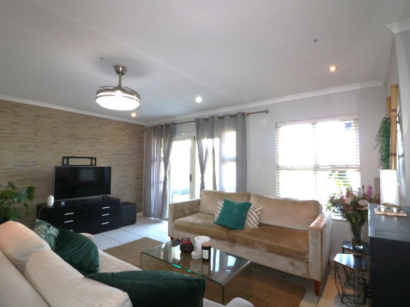 A bright living room featuring a textured accent wall, tiled flooring, recessed lighting, and a ceiling fan with direct access to an outdoor area.