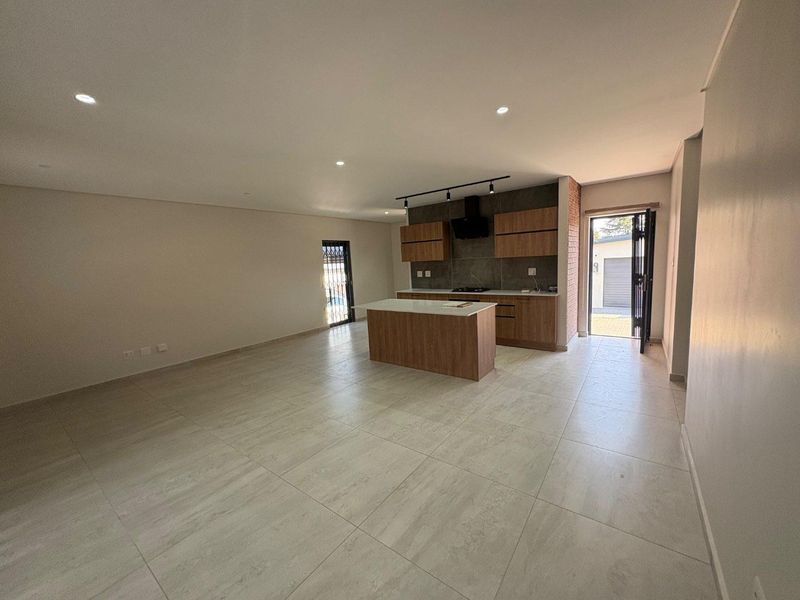 Spacious open-plan living area featuring a modern kitchen with a central island, sleek cabinetry, and large format floor tiles.