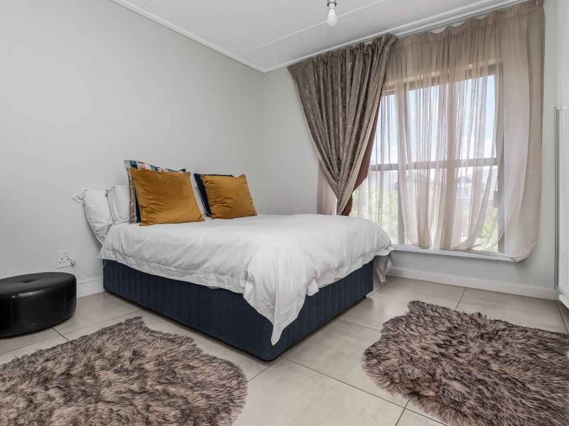 A well-lit bedroom featuring neutral tiled flooring, a large window with curtains, and built-in wardrobe storage.