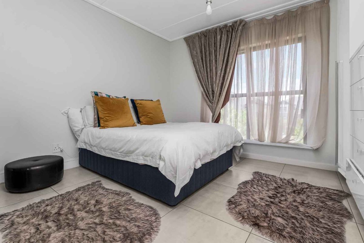 A well-lit bedroom featuring neutral tiled flooring, a large window with curtains, and built-in wardrobe storage.