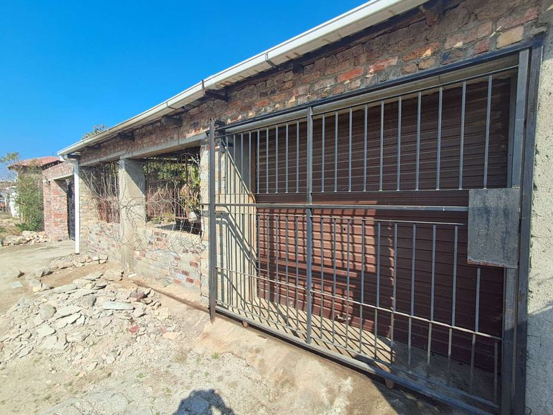 Exterior view of a garage structure featuring a metal roller door and security gate, currently in an unfinished state requiring renovation.