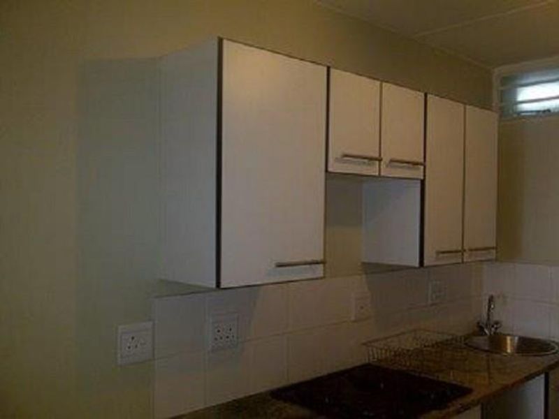 A functional kitchen area featuring white built-in cabinetry, a tiled backsplash, a stainless steel sink, and a built-in hob.