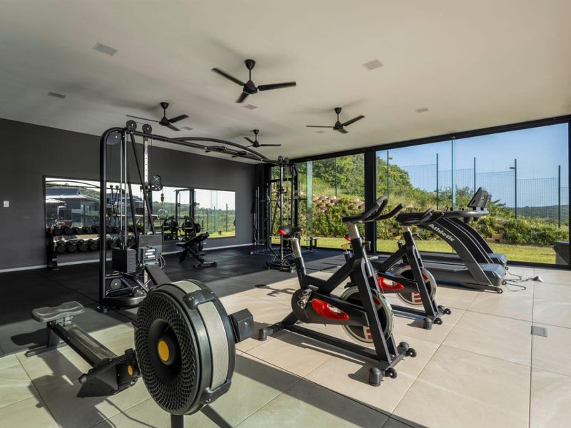 Modern, well-lit gym featuring floor-to-ceiling glass walls, mirrored surfaces, and a combination of tiled and rubber flooring, offering a bright and professional workout space.