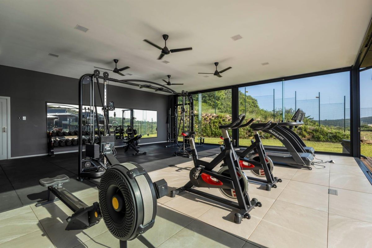Modern, well-lit gym featuring floor-to-ceiling glass walls, mirrored surfaces, and a combination of tiled and rubber flooring, offering a bright and professional workout space.