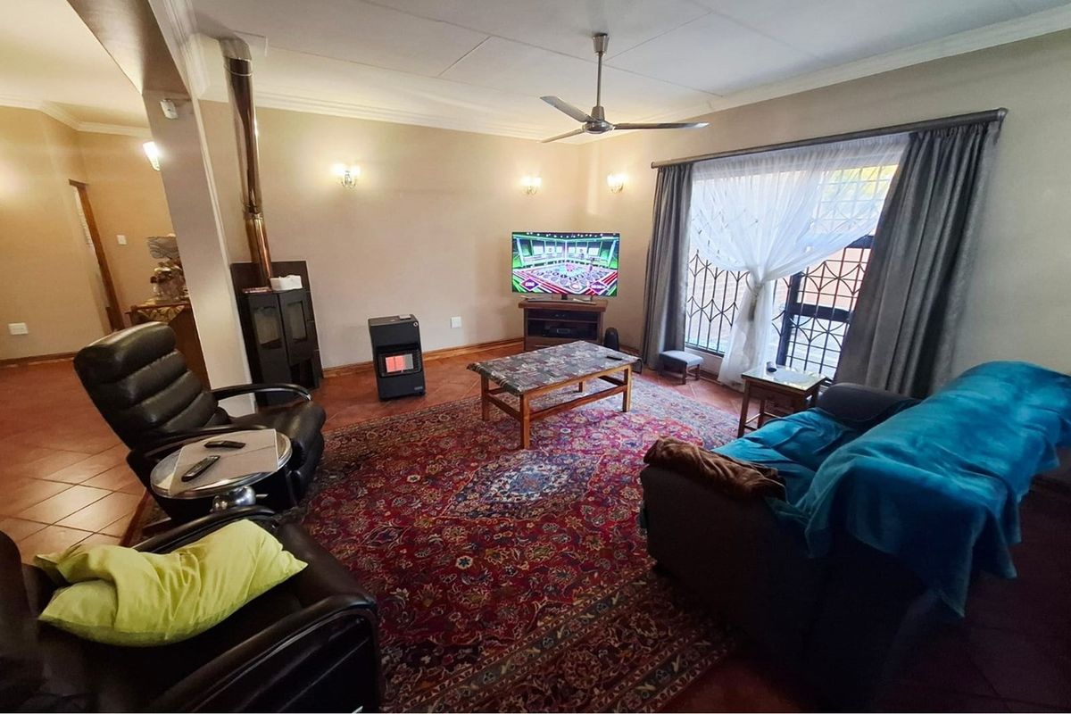 Spacious living room featuring tiled flooring, a built-in wood-burning fireplace, and a ceiling fan, with large windows providing natural light.