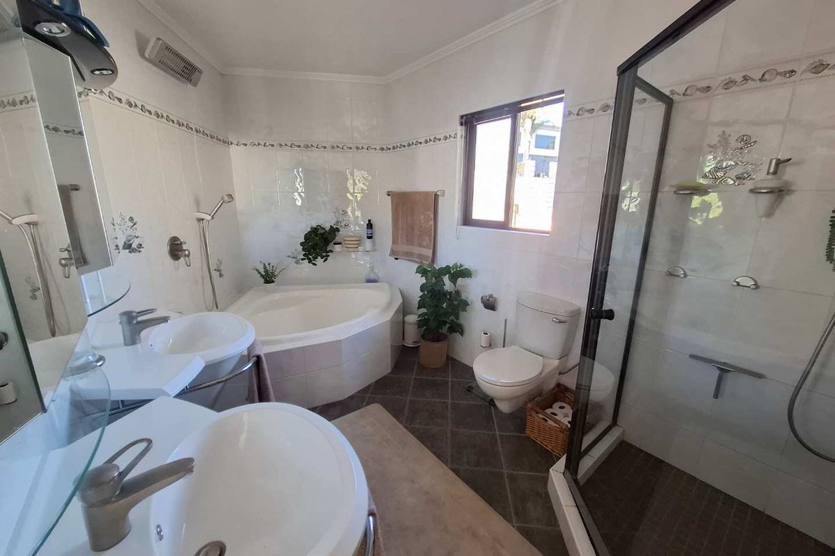 A functional bathroom featuring a corner bathtub, separate glass shower enclosure, and dual vanity sinks with tiled finishes throughout.