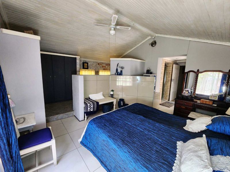 Spacious bedroom featuring a vaulted ceiling with fan, built-in storage, and a tiled partition wall separating the sleeping area from the dressing space.