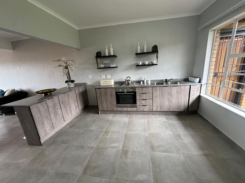 Modern kitchen featuring wood-look cabinetry, stainless steel sink, built-in oven, hob, and neutral tiled flooring with ample natural light.