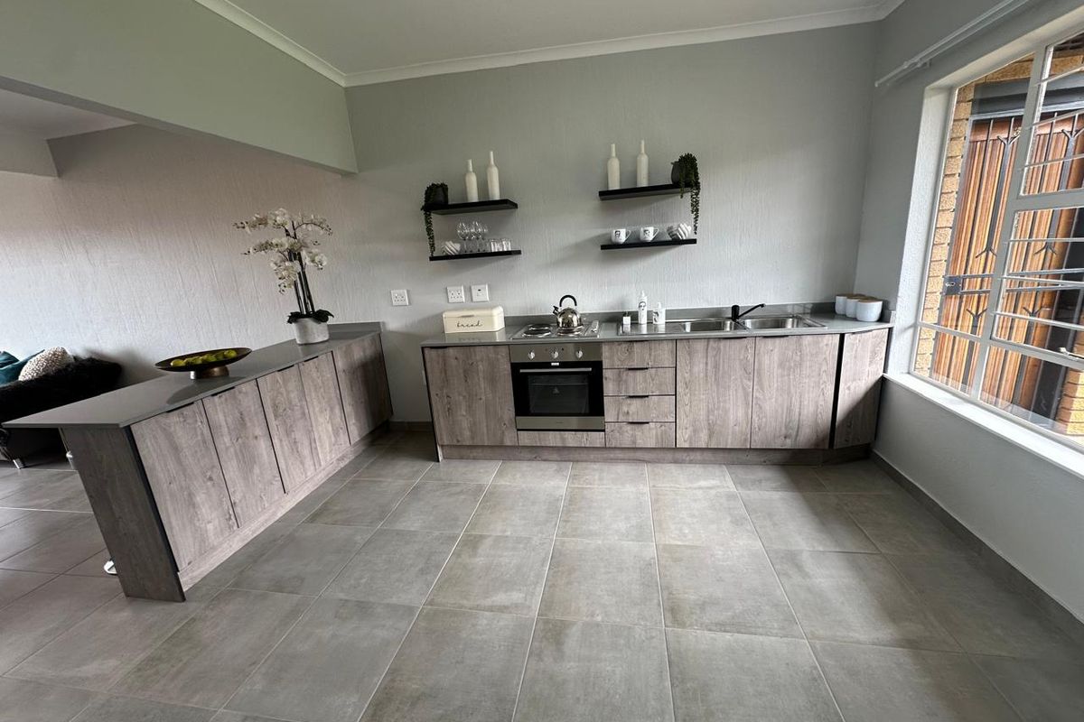 Modern kitchen featuring wood-look cabinetry, stainless steel sink, built-in oven, hob, and neutral tiled flooring with ample natural light.