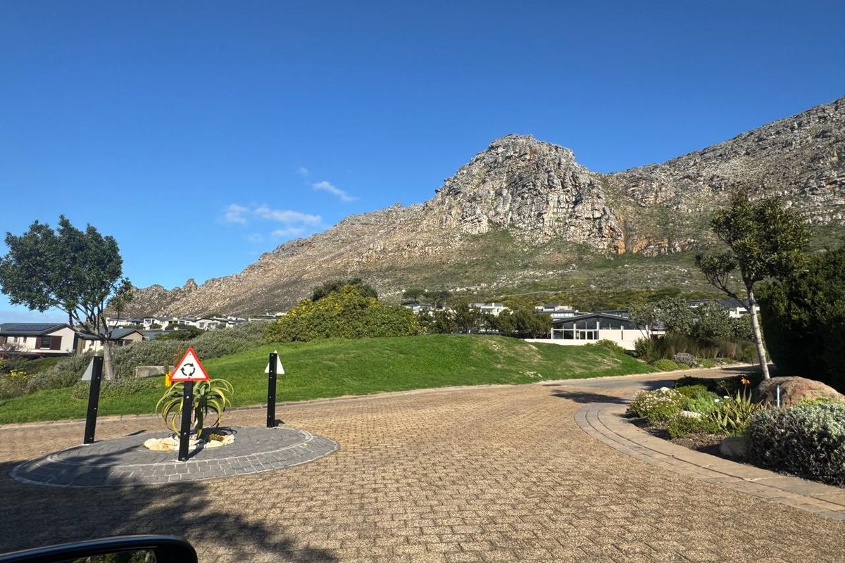 A scenic street view featuring a paved driveway, landscaped garden, and a prominent mountain backdrop in a well-maintained residential estate.