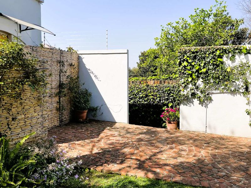 A private rear courtyard featuring classic brick paving, enclosed by boundary walls with integrated electric fencing and established greenery.