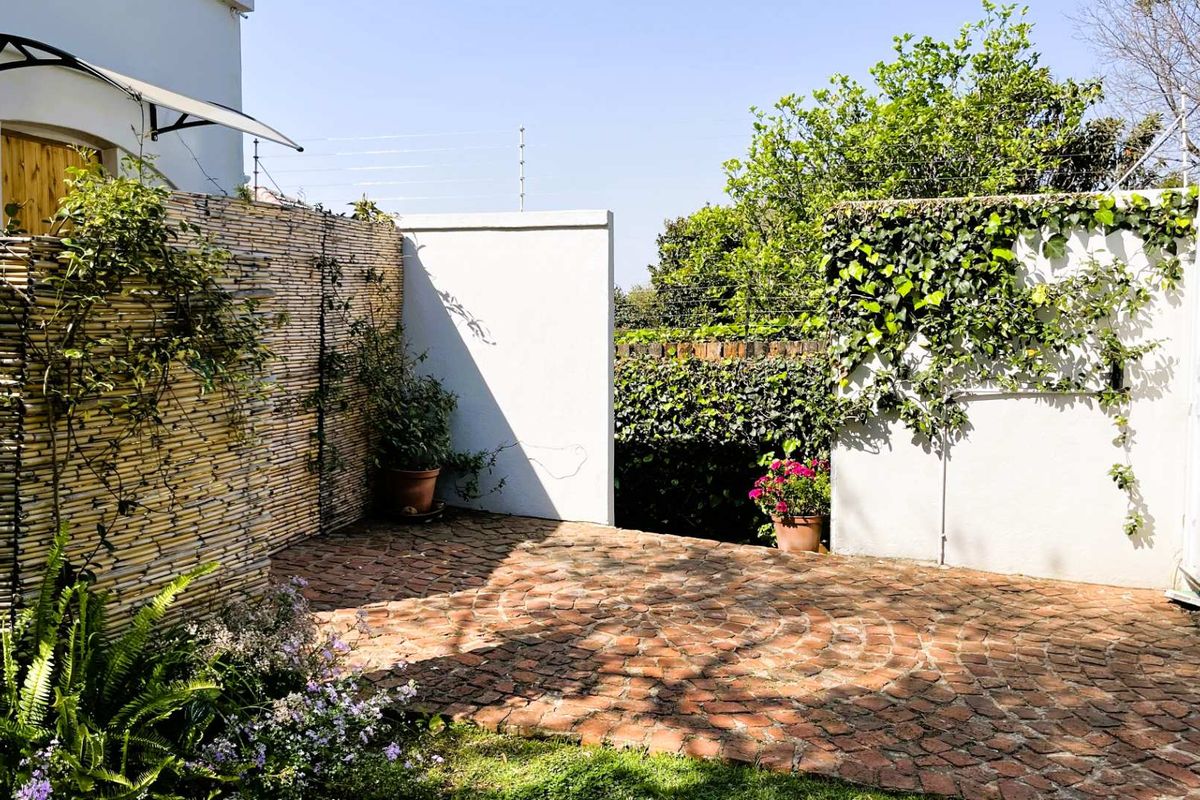 A private rear courtyard featuring classic brick paving, enclosed by boundary walls with integrated electric fencing and established greenery.
