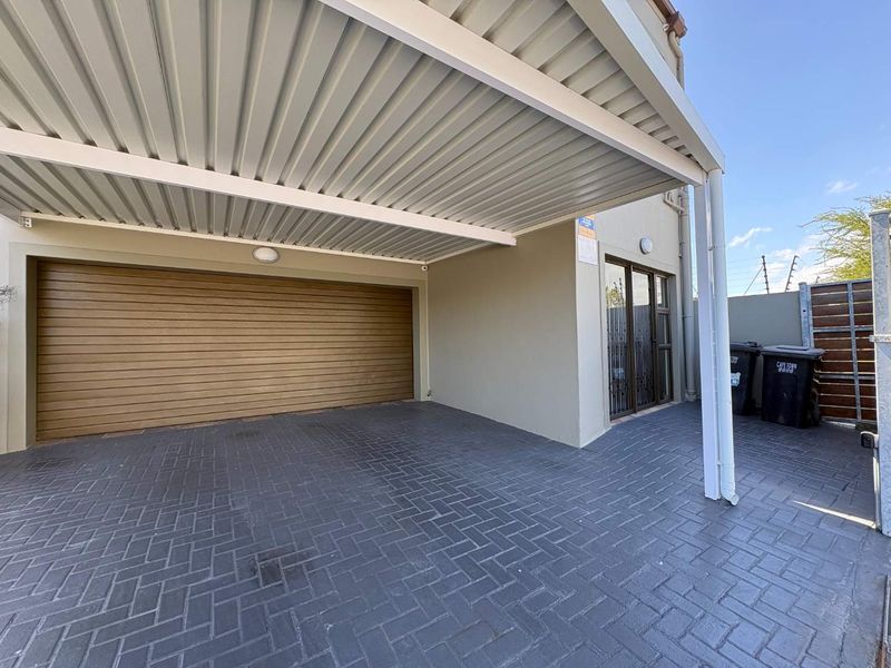 A clean, paved driveway area featuring a covered carport and a secure sectional garage door, providing convenient off-street parking.