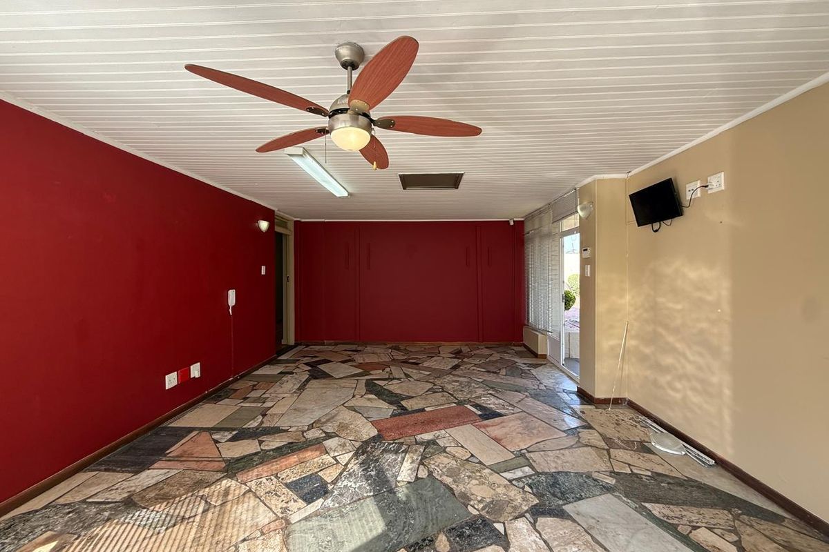 Spacious office area featuring unique stone tile flooring, a ceiling fan, and large sliding glass doors providing natural light.