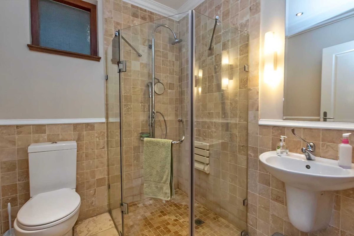 A compact bathroom featuring a glass-enclosed shower with stone tiling, a pedestal sink, and a standard toilet.