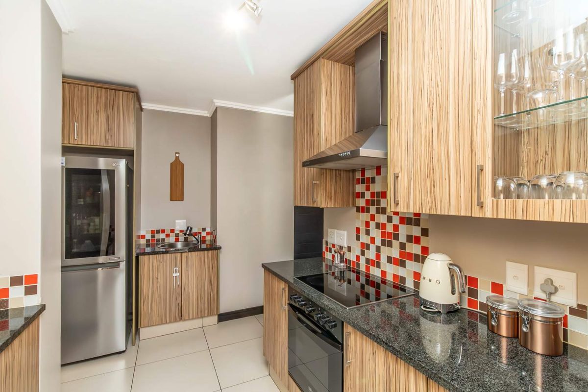Modern kitchen featuring wood-grain cabinetry, granite countertops, a mosaic tile backsplash, and integrated stainless steel appliances.