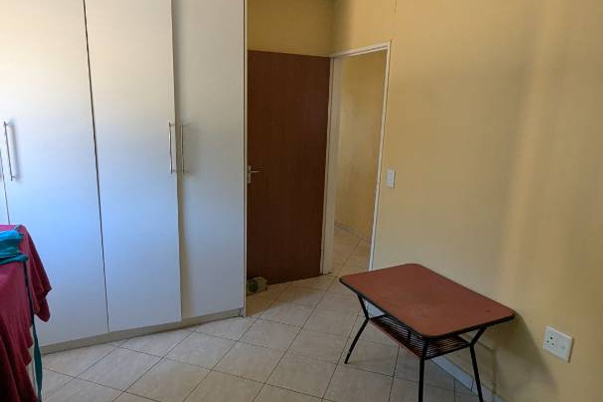 A bedroom featuring built-in cupboards, tiled flooring, and a doorway leading to an adjacent space.