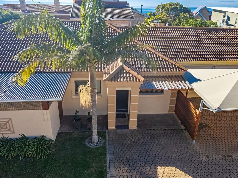 Aerial view of the townhouse front facade featuring a paved driveway, covered carport, and a well-maintained entrance area with tiled roofing.