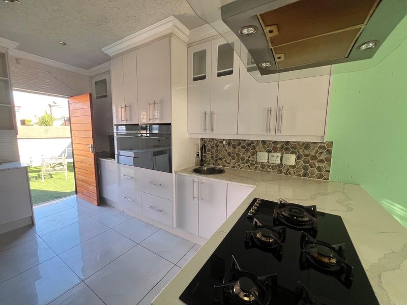 Modern kitchen featuring white cabinetry, stone countertops, gas hob, built-in oven, and a stylish hexagonal tile backsplash with direct access to the rear patio.