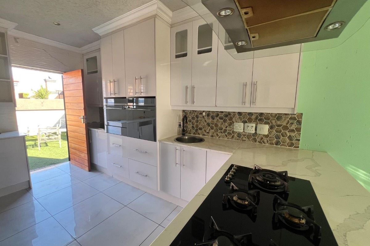 Modern kitchen featuring white cabinetry, stone countertops, gas hob, built-in oven, and a stylish hexagonal tile backsplash with direct access to the rear patio.