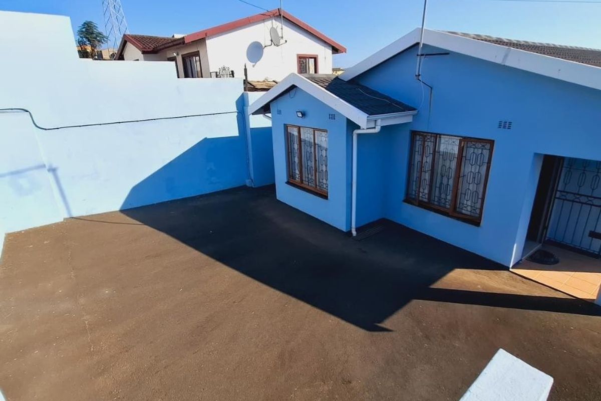 A view of the rear exterior of the house featuring a paved courtyard area and secure window bars.