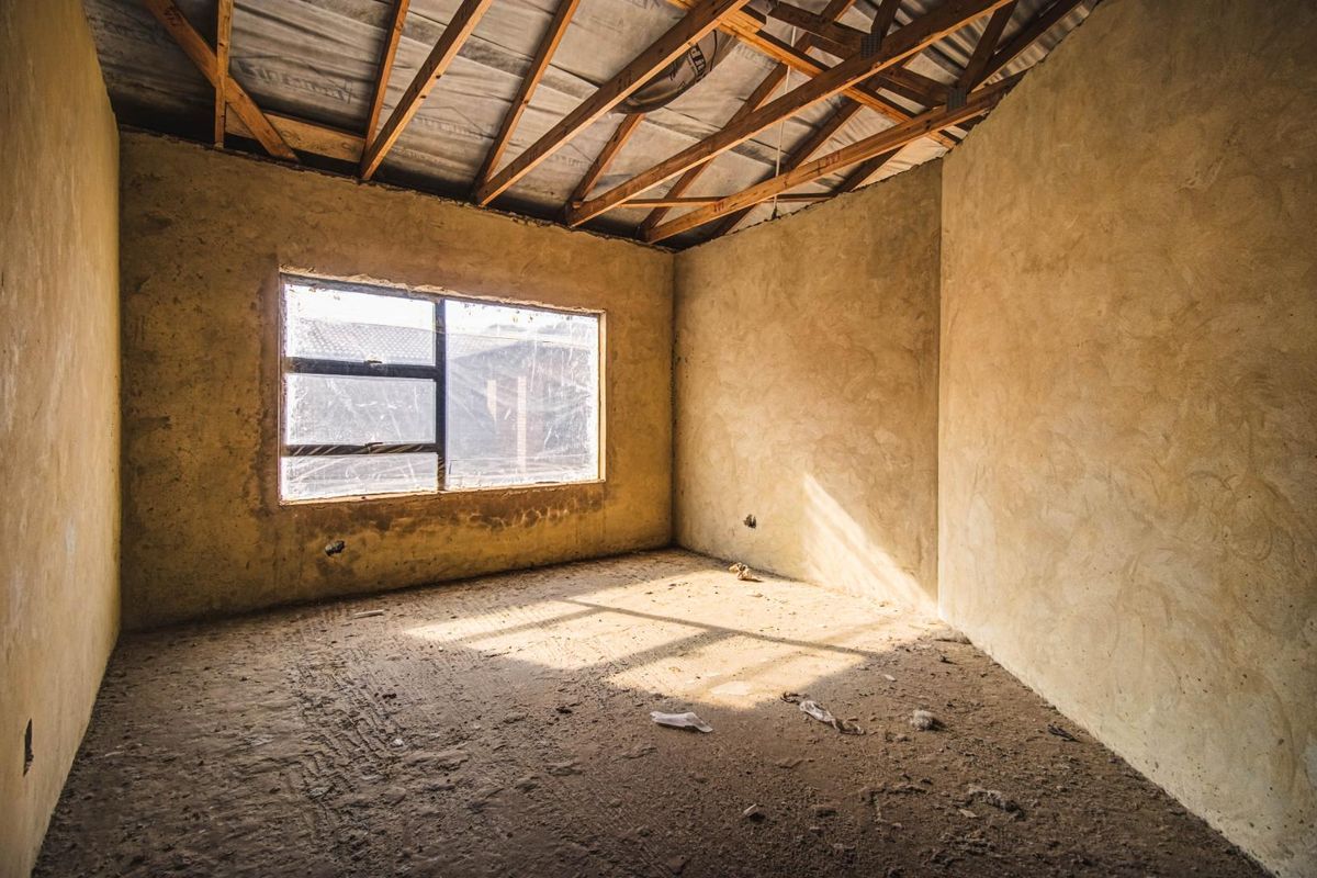 An unfinished bedroom interior featuring exposed timber roof trusses, plastered walls, and a concrete floor, offering a blank canvas for renovation.