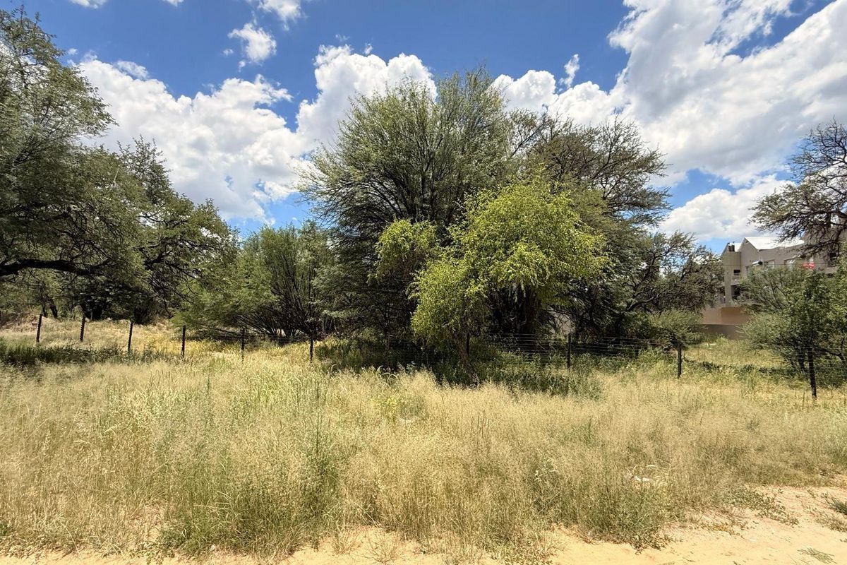 A view of a vacant residential plot featuring mature trees, natural grass, and perimeter wire fencing.