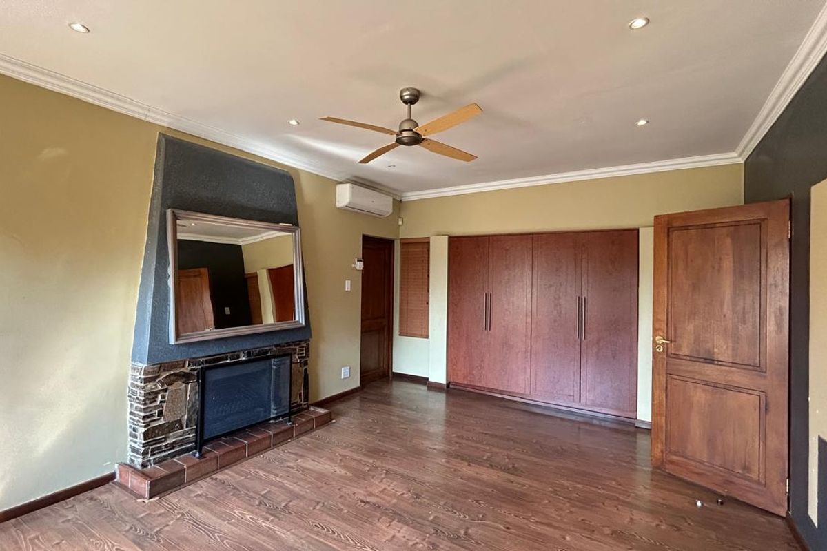 Spacious bedroom featuring built-in wooden cupboards, a stone-clad fireplace, ceiling fan, air conditioning unit, and laminate flooring.