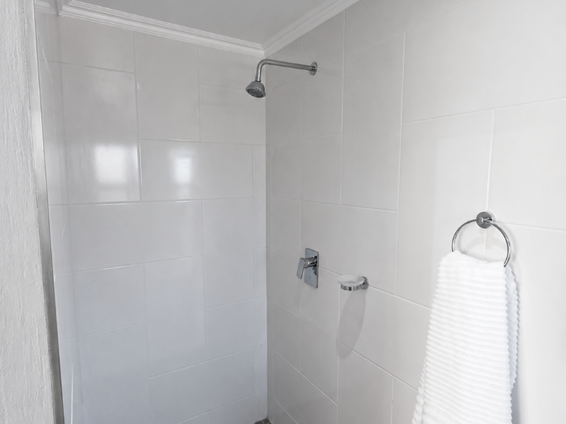 A clean, modern walk-in shower featuring white wall tiles, a grey mosaic tiled floor, and chrome fixtures.