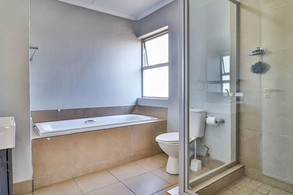 A functional bathroom featuring a built-in bathtub, a separate glass-enclosed shower, a wall-mounted vanity basin, and neutral ceramic tiling throughout.
