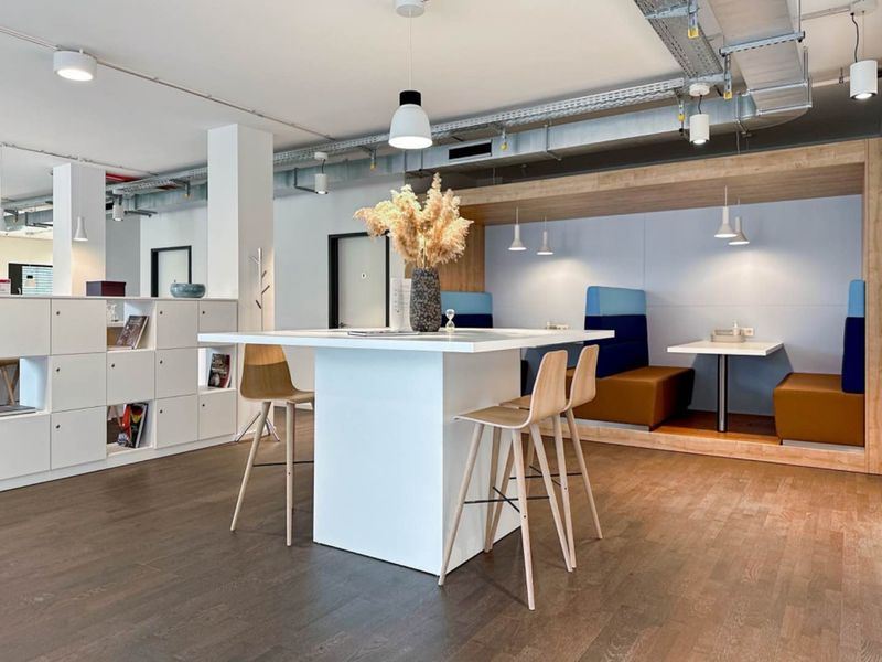 Modern open-plan office breakout area featuring exposed industrial ceiling ducting, built-in booth seating, and integrated storage cabinetry with high-quality hardwood flooring.
