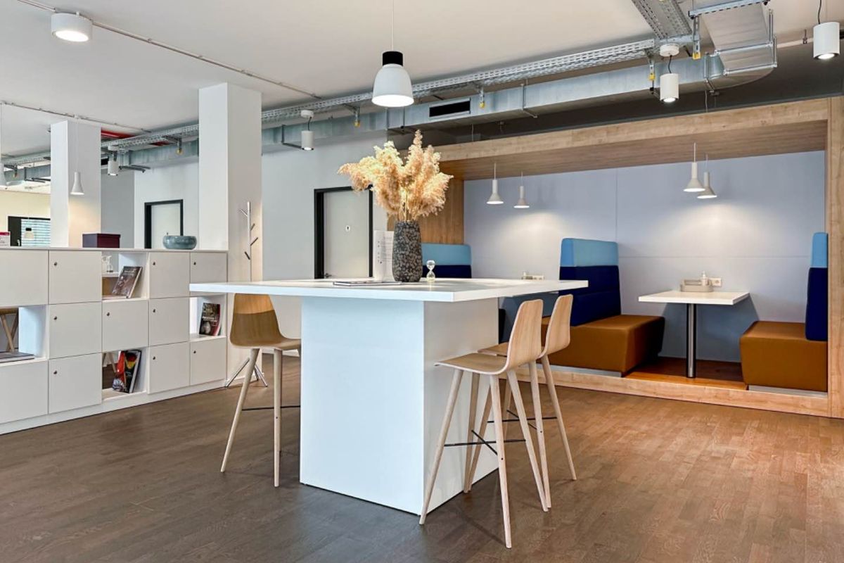 Modern open-plan office breakout area featuring exposed industrial ceiling ducting, built-in booth seating, and integrated storage cabinetry with high-quality hardwood flooring.