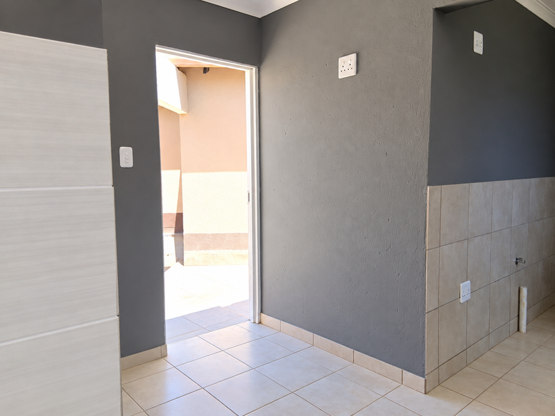 A clean, empty hallway featuring neutral tiled flooring, grey painted walls, and a doorway leading to an outdoor area.