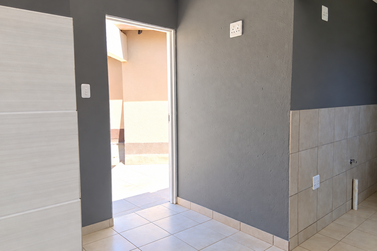 A clean, empty hallway featuring neutral tiled flooring, grey painted walls, and a doorway leading to an outdoor area.