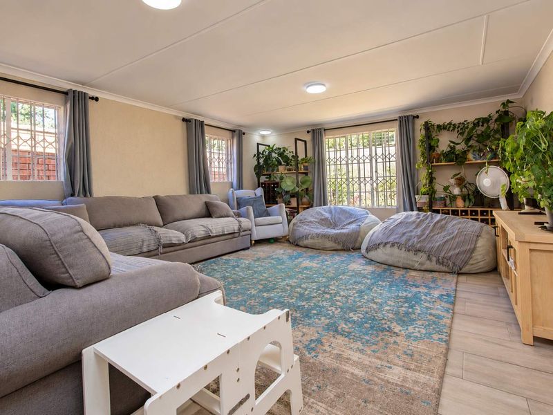 A spacious living room featuring tiled flooring, large windows with security bars, and recessed ceiling lighting, offering a comfortable and functional family living space.