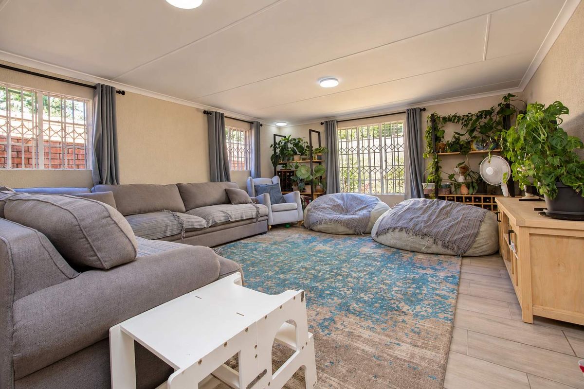 A spacious living room featuring tiled flooring, large windows with security bars, and recessed ceiling lighting, offering a comfortable and functional family living space.
