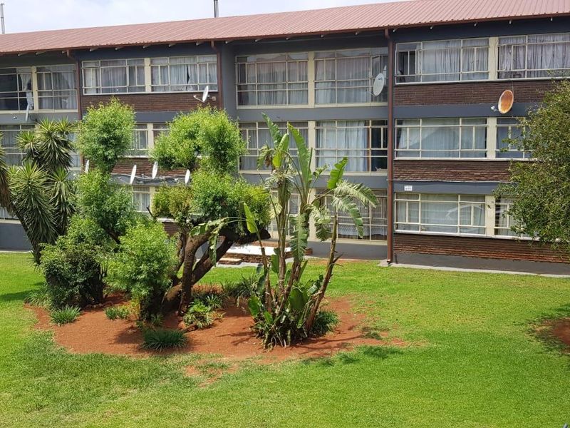 A view of the rear elevation of a multi-story apartment building featuring brick cladding, large windows, and a well-maintained communal garden area.