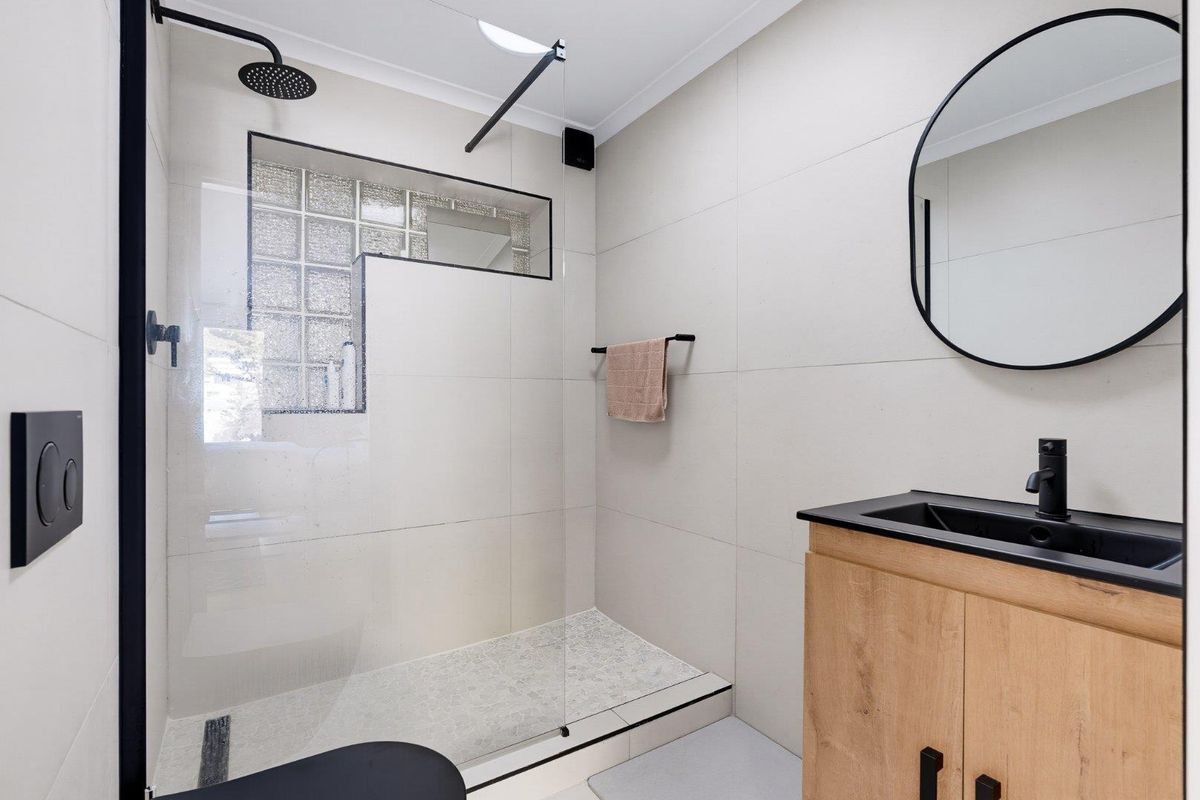 Modern bathroom featuring a walk-in shower with a rain shower head, glass block window, and a contemporary vanity with black fixtures.
