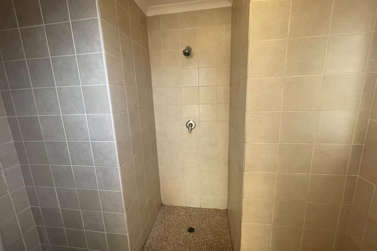 A functional shower enclosure featuring neutral wall tiles and a mosaic tiled floor, currently in need of cosmetic updates.