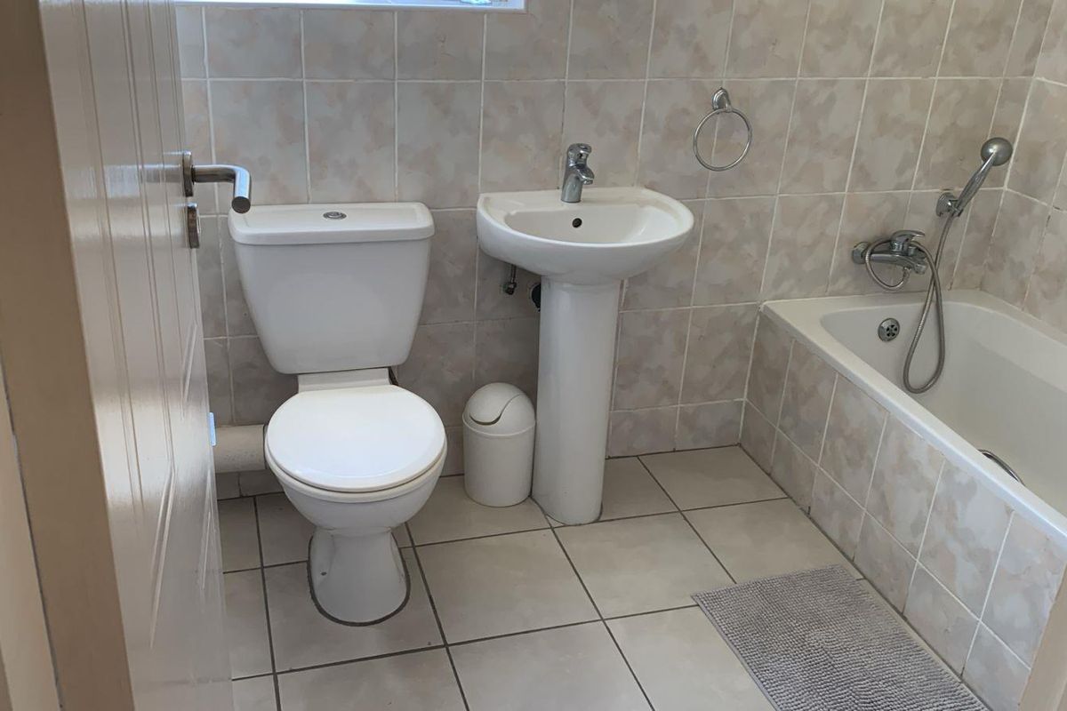 A functional bathroom featuring a pedestal basin, toilet, and a bathtub with a handheld shower attachment, finished with neutral wall and floor tiles.
