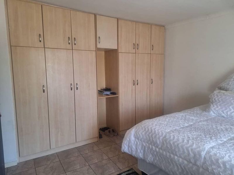 A bedroom featuring extensive light wood-finish built-in cupboards and tiled flooring, providing ample storage space.