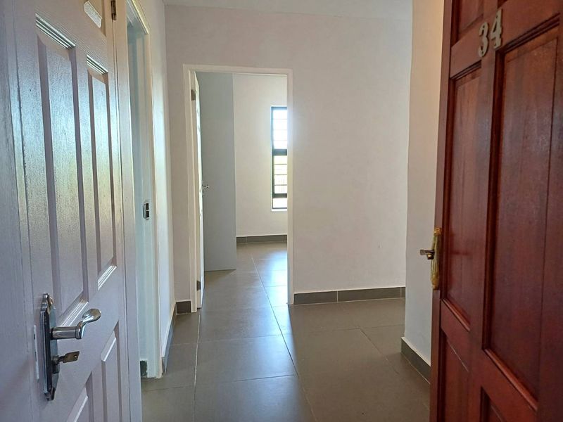 A clean, empty hallway featuring neutral tiled flooring and multiple internal doorways leading to adjacent rooms within the apartment.