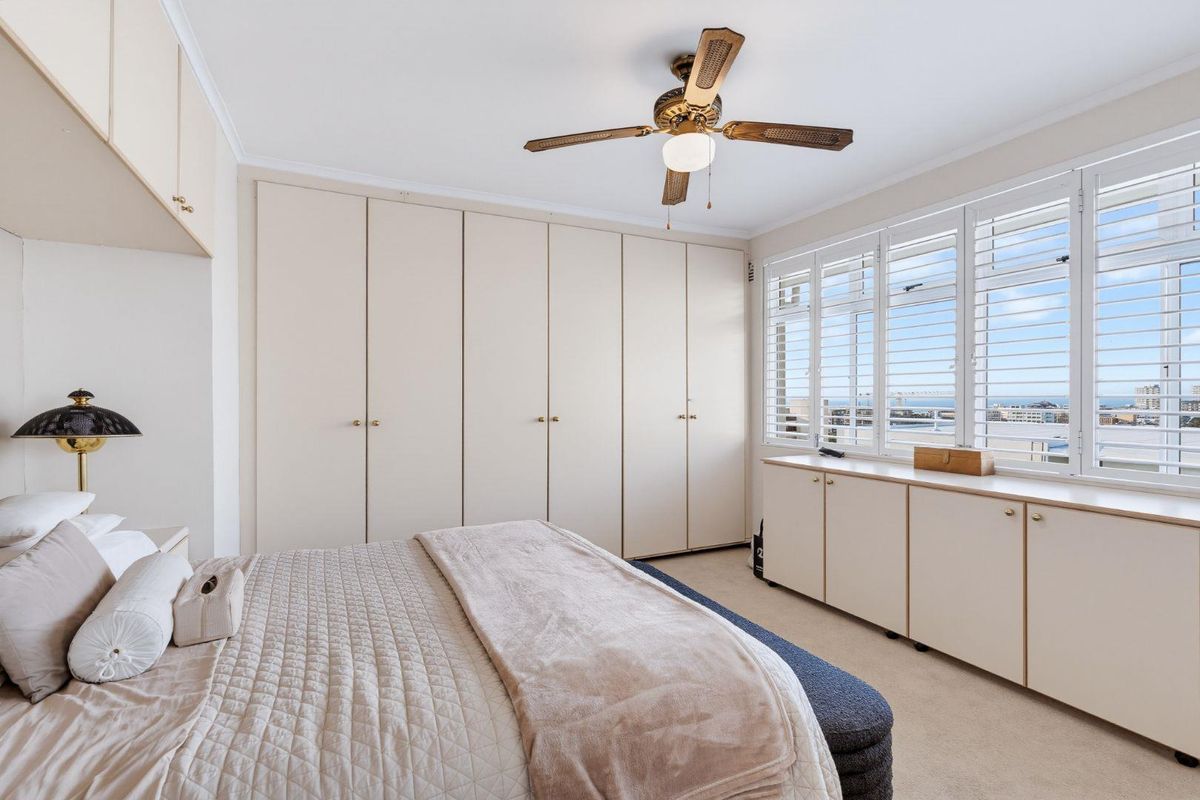A well-maintained bedroom featuring extensive built-in wardrobe storage, custom cabinetry, plantation shutters, and a ceiling fan with views of the surrounding area.
