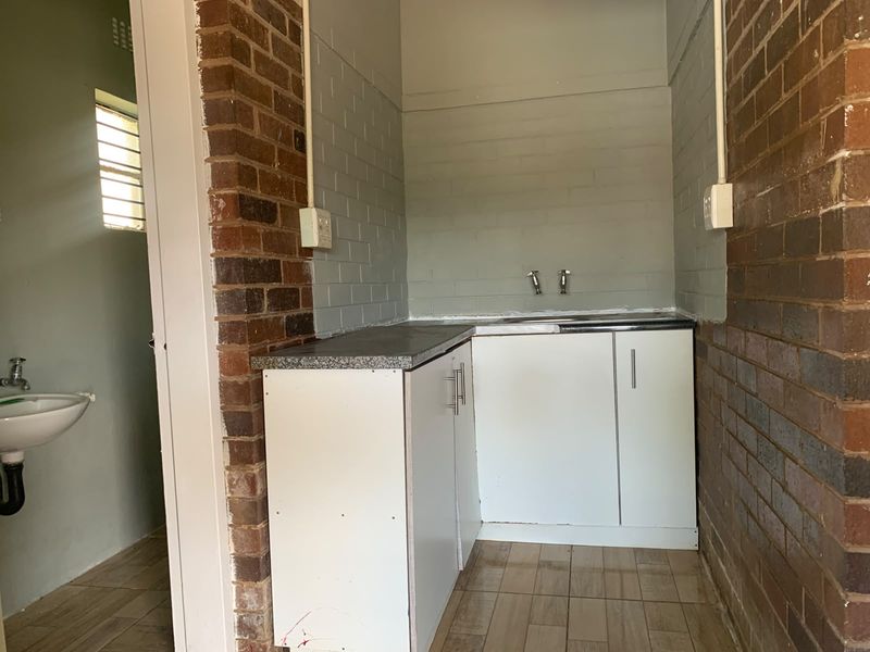 A functional laundry area featuring built-in cabinetry, a stainless steel sink, and exposed brick walls, providing a practical utility space.